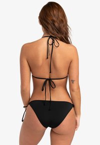 Svart bikini-set med halterneck och knytband samt minimalt täckande bikiniunderdelar, tillverkad av ett mjukt, elastiskt material.