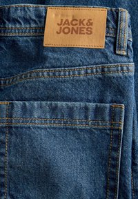 Сини дънки с видими шевове и кафява кожена емблема с марката Jack & Jones над задния джоб.