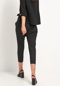 Černé zkrácené kalhoty s upraveným střihem, s hladkou texturou a jemným leskem. V kombinaci s černými sandály na blockovém podpatku.