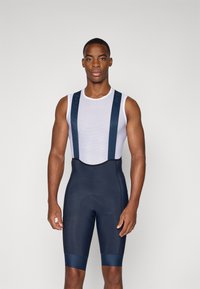 Pantalones cortos de ciclismo para hombres en navy con un top de malla blanca. Cuenta con tirantes anchos y un forro acolchado para mayor comodidad. Tejido suave y elástico.