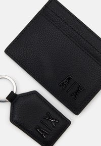 Schwarzes strukturiertes Lederkartenetui und Schlüsselanhänger mit eingeprägten "AIX"-Buchstaben. Rundes Schlüsselring an dem Anhänger befestigt.