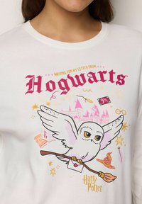 Búho blanco llevando una carta y una escoba vuela frente al castillo de Hogwarts con símbolos mágicos, texto "Esperando mi carta de Hogwarts."