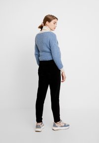 Lyseblå fuzzy strikket sweater med cremefarvet krave, parret med sorte fløjl-bukser og sneakers med blå accenter. Modellen står med ryggen til.
