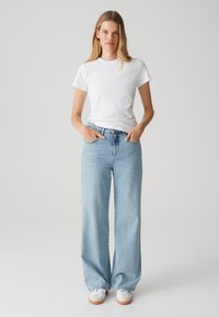 T-shirt bianco a maniche corte abbinato a jeans a gamba larga di colore azzurro chiaro. I jeans presentano un design classico a cinque tasche e sono leggermente strappati.