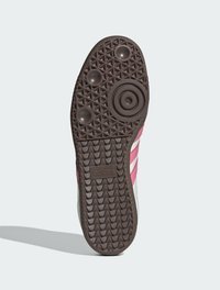Suola di scarpa Adidas caratterizzata da una gomma marrone testurizzata con motivi di grip e tre strisce rosa su uno sfondo bianco. Logo impresso.
