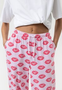 Loungewear broek van zacht roze stof met een herhaald patroon van rode lippen. Elastische tailleband met een trekkoord en zijzakken.