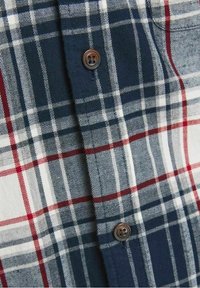 Gros plan d’un tissu à carreaux bleu, blanc et rouge avec deux boutons marron cousus dessus.