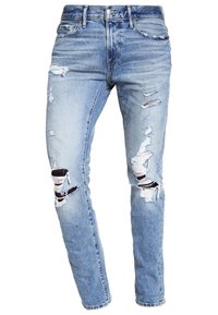 Jeans desgastados de color azul claro con múltiples roturas en los muslos y las rodillas, estilo de cinco bolsillos y cierre de botón en la cintura.