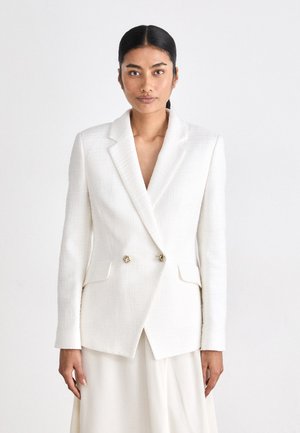 White double-breasted blazer in textured fabric, featuring notch lapels, gold-tone hardware, and two front pockets. Smooth, structured design.