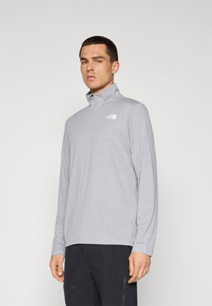 Helles grauer Langarmpullover mit einem halben Reißverschluss und hohem Kragen, mit einem weißen Logo auf der linken Brust. Weicher, strukturierter Stoff.