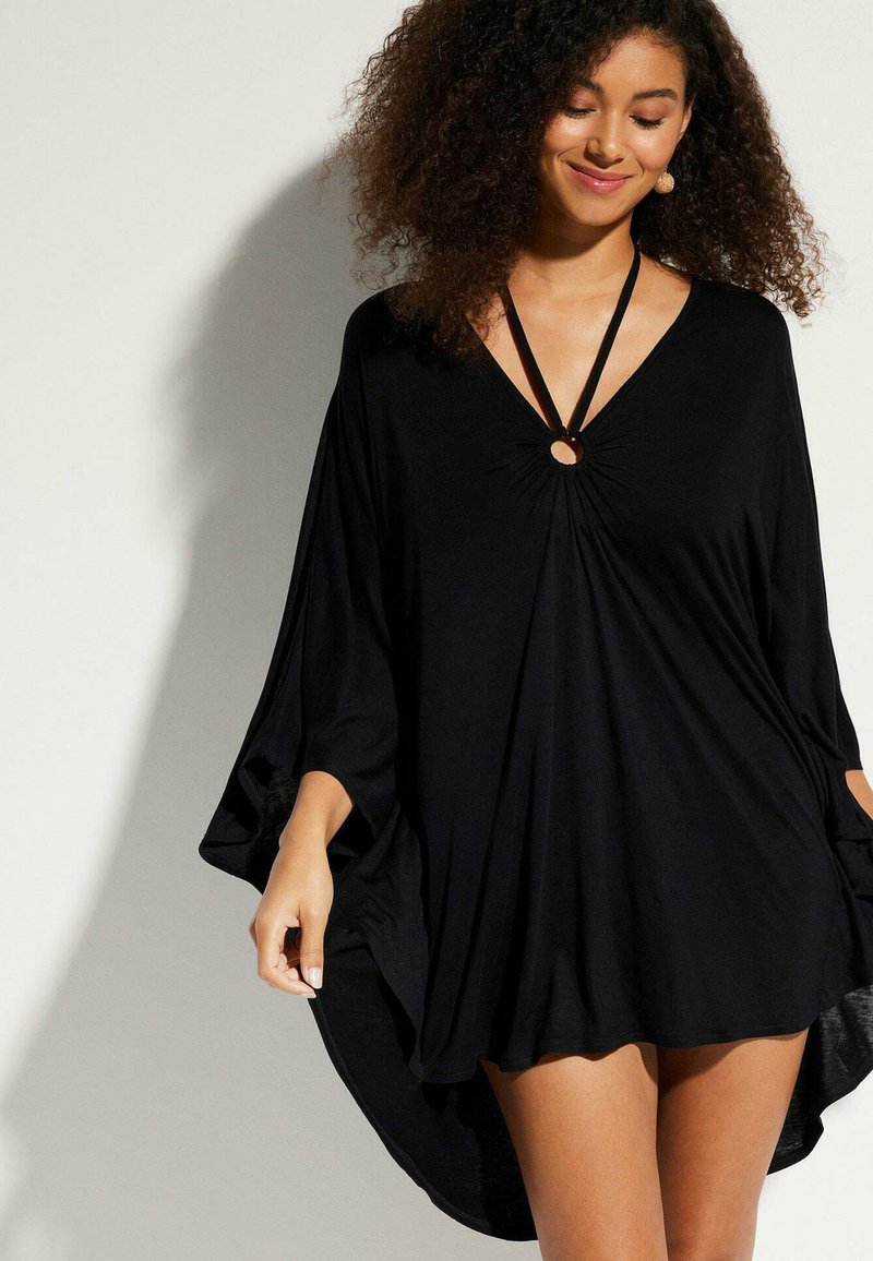 Robe noire avec un décolleté en V, des manches longues et une taille cintrée, mettant en avant un accent circulaire. Tissu doux et fluide avec une coupe ample.