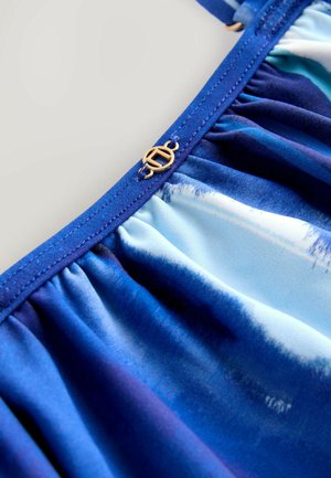 Blauer Stoff mit einem Farbverlaufsmuster, das von hellen zu dunklen Tönen reicht. Gesammeltes Design mit einem goldenen runden Metallelement.