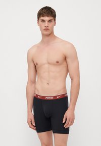Sorte bomulds Nike boxer briefs med en rød talje, der har brandlogoet, glat stof, tætsiddende design og længde til midten af låret.