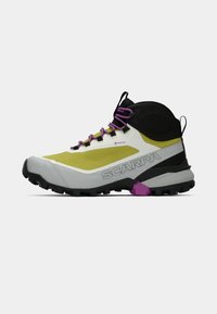 Zapatos de senderismo de corte medio en amarillo, negro y gris. Presentan un logo de Gore-Tex, cordones morados y una suela robusta con tacos profundos para mayor tracción.