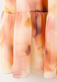 Tissu transparent avec des volants froncés dans des tons doux pêche, rose et orange avec un motif floral semblable à de l'aquarelle sur un vêtement fluide.