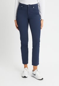 Navy blue stretch pants with a slim fit, featuring two front pockets, a button closure, and cuffed hems. Paired with white sneakers.