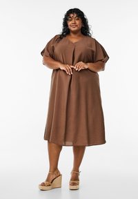 Braunes knielanges Kleid mit lockerer Passform, kurzen Ärmeln, V-Ausschnitt und strukturiertem Finish. Kombiniert mit hellbraunen Keilsandalen.