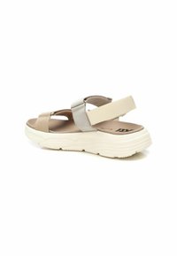 Sandalias de tela beige y plateadas con suela blanca gruesa, que cuentan con tiras cruzadas y una correa elástica en la parte trasera para un ajuste seguro. Plantilla texturizada.