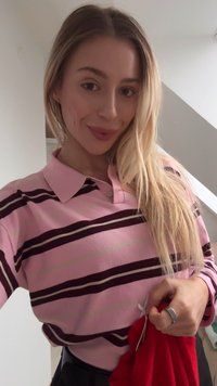 Pink polo shirt with maroon and green stripes; short sleeves; collar with two buttons; holding a red fabric in the right hand.