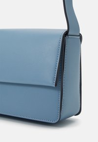 Světle modrá kožená crossbody taška s klopou a viditelným švem podél okrajů a připojení popruhu.