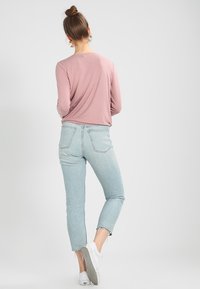 Pitkät hihat, vaaleanpunainen paita yhdistettynä vaaleansinisiin korkeavyötäröisiin farkkuihin, joissa on lyhennetty helma ja repaleiset reunat. Valkoiset lenkkarit täydentävät asua.