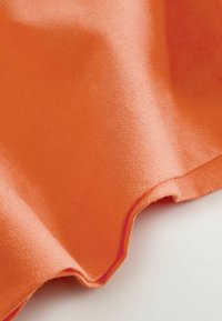 Gros plan d'un tissu orange doux avec une texture tissée visible et de légers plis sur une surface claire.