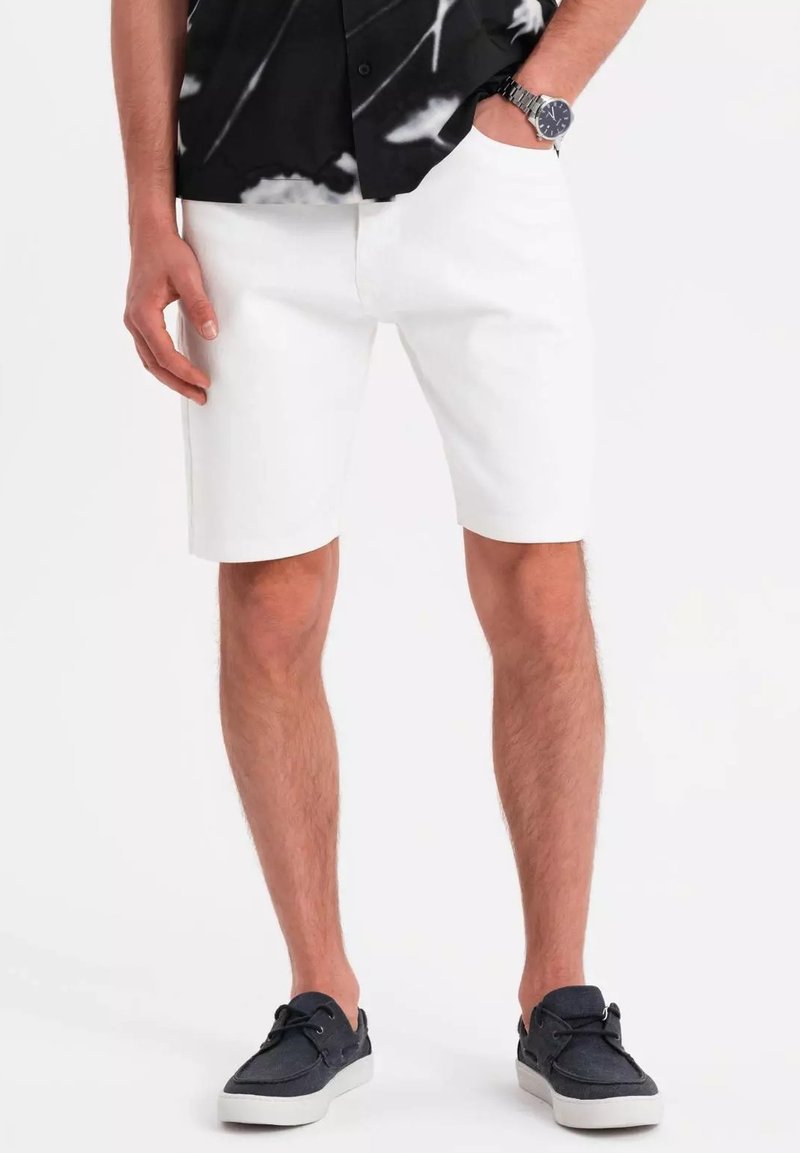 Pantalones cortos blancos con un diseño de pierna recta, hechos de una tela de textura suave. Llevados con una camisa negra estampada y zapatillas oscuras.