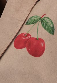 Tessuto beige con un design dipinto di due ciliegie rosse con foglie verdi, che presenta una trama liscia e colori vivaci.