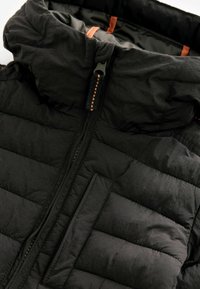 Giacca imbottita nera con colletto alto, zip centrale e accenti arancioni. Presenta una texture trapuntata e una tasca anteriore.