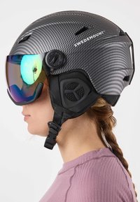 Carbon fiber ski helmet in matte black with a mirrored visor. Features adjustable strap and ventilation openings. Tight-fitting design.