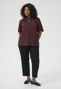 Maroon, short-sleeve top with textured fabric and tie neckline. Paired with black, straight-leg pants and black flats.