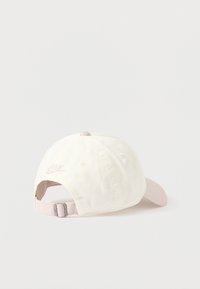 Biały bawełniany baseballowy kaszkiet z jasno różowym zakrzywionym daszkiem, z małym różowym haftowanym logo Nike z tyłu. Regulowane zapięcie na pasku.