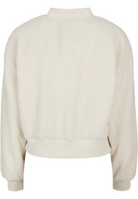 Kremfarget kunstpelsjakke med lange ermer, rund krage og elastiske mansjetter og kant. Myk tekstur med en avslappet passform.
