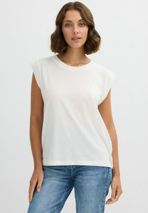 Camiseta sin mangas blanca de tejido suave, con escote redondo y ligeras hombreras, combinada con unos vaqueros de mezclilla azul claro.