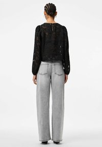 Melna caurspīdīga blūze ar ziedu rakstu un pūsta piedurkņu dizainu, kopā ar augstās vidukļa pelēkām plata kāju džinsa biksēm. Redzams aizmugurējais cauruma detaļas elements.