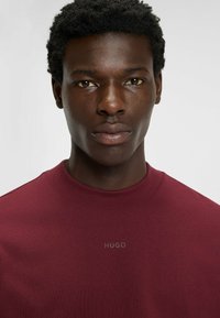 Bordeaux sweatshirt met ronde hals en het reliëflogo "HUGO" op de borst. Glad stoftextuur en korte mouwen. Eenvoudig, klassiek ontwerp.