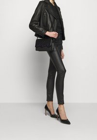 Chaqueta de biker de cuero negro, top negro ajustado, pantalones skinny brillantes negros, y tacones de aguja negros. Bolso con acentos púrpuras y tachuelas.