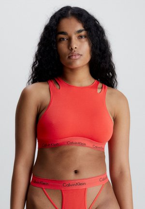 Crvena sportska brusa s rezovima na ramenima i elastičnom trakom s logotipom "Calvin Klein" u crnoj boji. Glatka tkanina s prilagođenim oblikom.