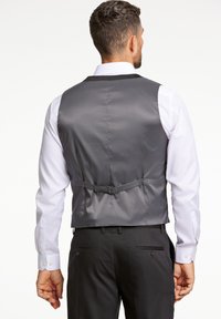 Gilet grigio in satin con un design aderente, cinturino posteriore regolabile e texture liscia, indossato sopra una camicia bianca a maniche lunghe.