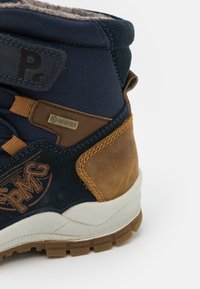 Høye støvler med marineblått stoff og brune lærdetaljer. Har en teksturert gummisåle og en vanntett Gore-Tex-etikett.
