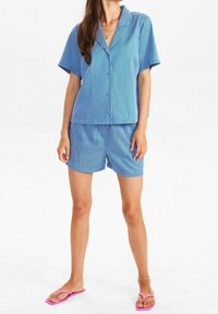 Blå och vit randig kortärmad skjorta med matchande shorts. Lätt tyg, avslappnad passform, slät textur, detaljerade knappar. Rosa flip-flops.