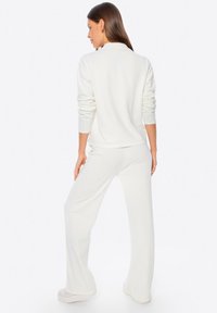 Sudadera blanca de canalé con cuello y mangas largas, combinada con pantalones acampanados a juego. Tejido suave, diseño minimalista, sin patrones visibles.