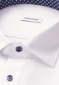 Camicia bianca con tessuto a trama, colletto blu navy con pois blu e bottoni scuri. Etichetta del brand: Seidensticker.
