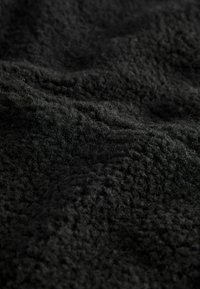 Čierna fleecová tkanina s mäkkým, textúrovaným povrchom. Materiál je nadýchaný a mierne pokrčený, s jednotnou tmavou farbou.