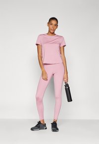 Maglietta atletica rosa chiaro e leggings abbinati, entrambi aderenti, con una finitura opaca. Scarpe da ginnastica nere e una borraccia nera completano l'outfit.