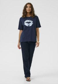 Marineblaue Baumwoll-T-Shirt mit einem großen weißen Grafik von Lippen auf der Vorderseite. Kombiniert mit dunklen Jeans und schwarzen Sandalen.