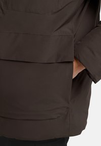 Braune Oberbekleidung mit einer glatten, matten Oberfläche. Verfügt über eine Fronttasche und ein lässiges Design. Einfache Naht entlang der Kanten.