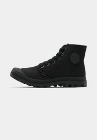 Svarte høye sneakers med kanvasutvendig, gummitoe-kap og teksturert såle. Har metalløye og en sirkulær logo-detail på siden.