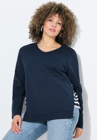 Marineblaues Sweatshirt mit langen Ärmeln, rundem Ausschnitt und gestreiften Seitenelementen. Weicher Stoff mit lässiger Passform. Kombiniert mit hellblauen Jeans.