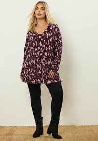 Túnica de manga larga en color marrón oscuro con patrones florales en rosa, combinada con pantalones ajustados negros y botines negros. Tejido texturizado.